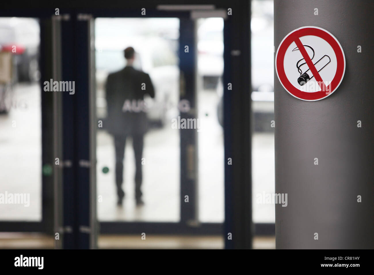 No smoking sign and a man smoking in front of an office building Stock Photo