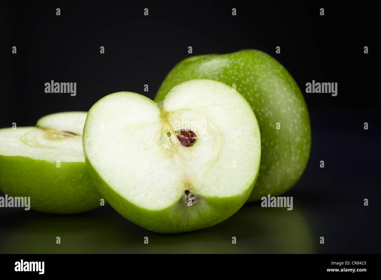 Two green Granny Smith apples, one whole apple and one apple cut in half, on black glass plate Stock Photo