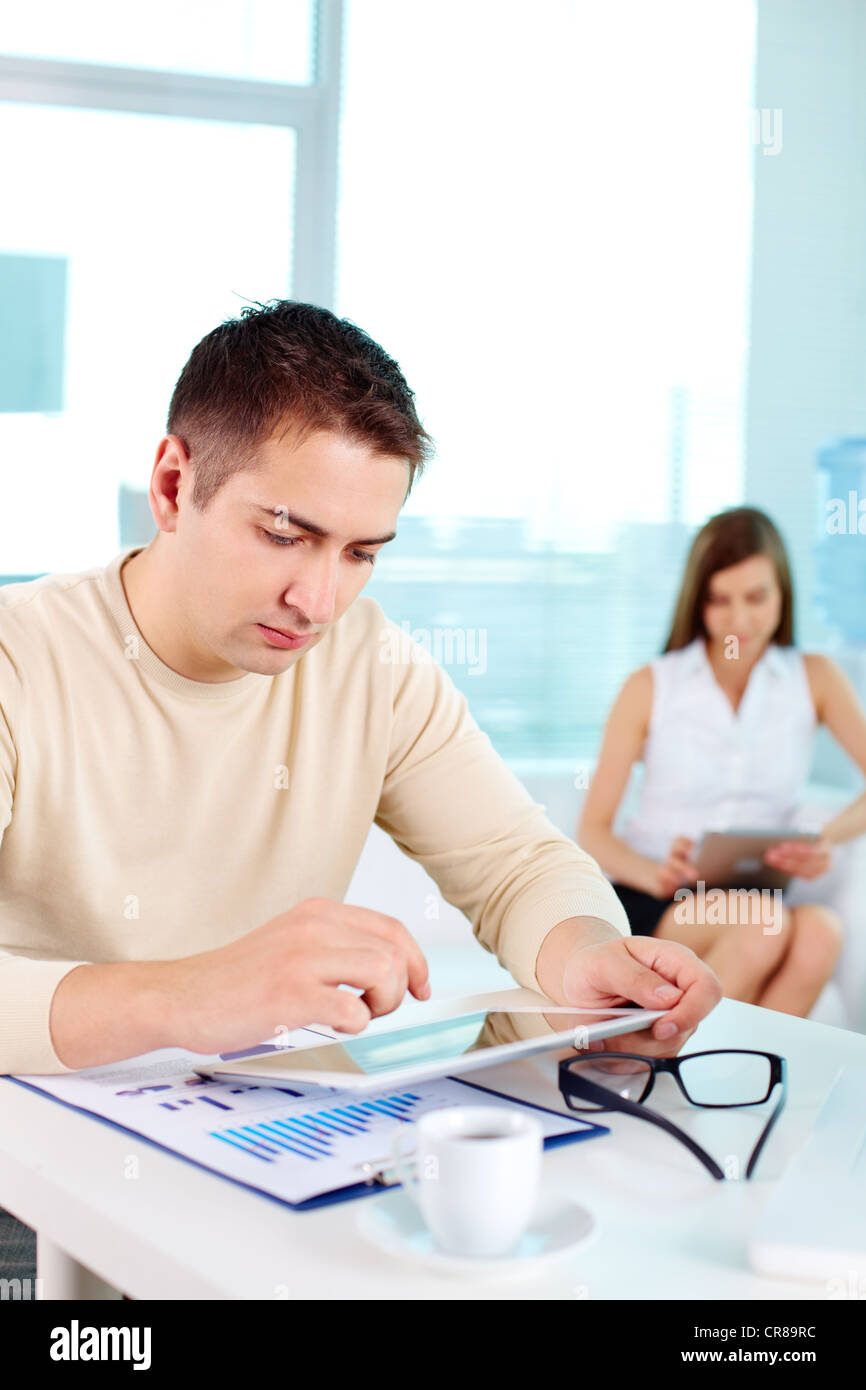 Serious businessman working with digital tablet at workplace with his colleague on background Stock Photo