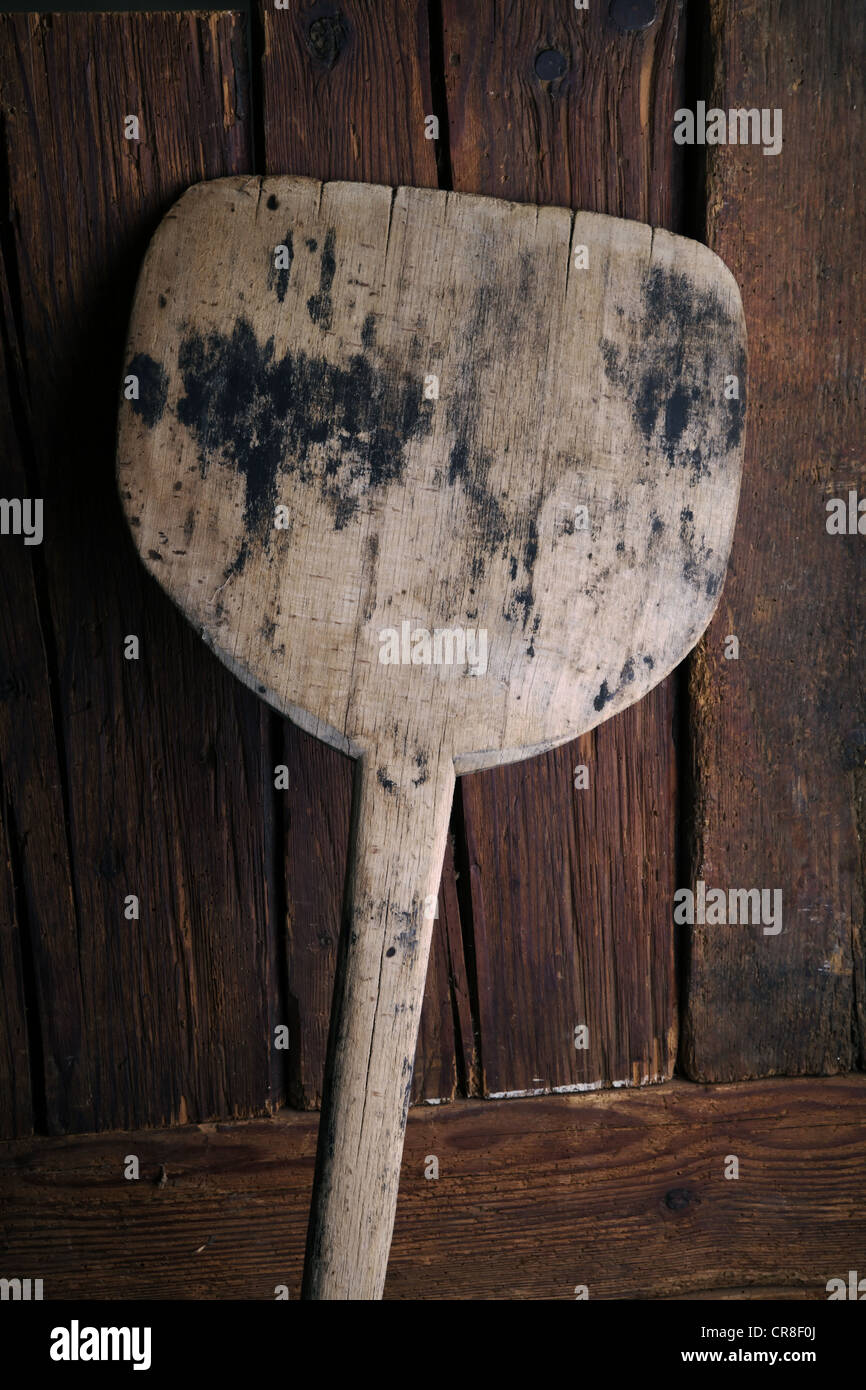 Old bread scoop leaning against a rustic wooden wall Stock Photo