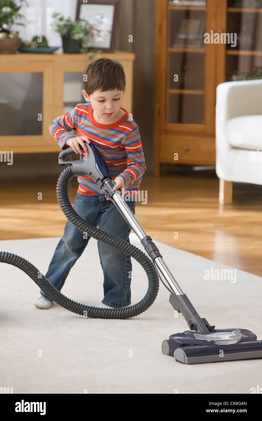 Boy using vacuum cleaner on rug Stock Photo