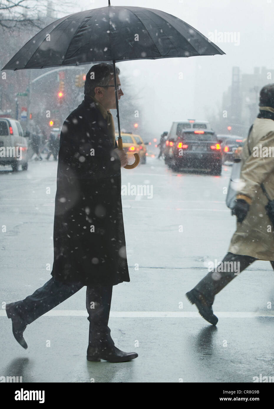 Mature man crossing city street in rain Stock Photo