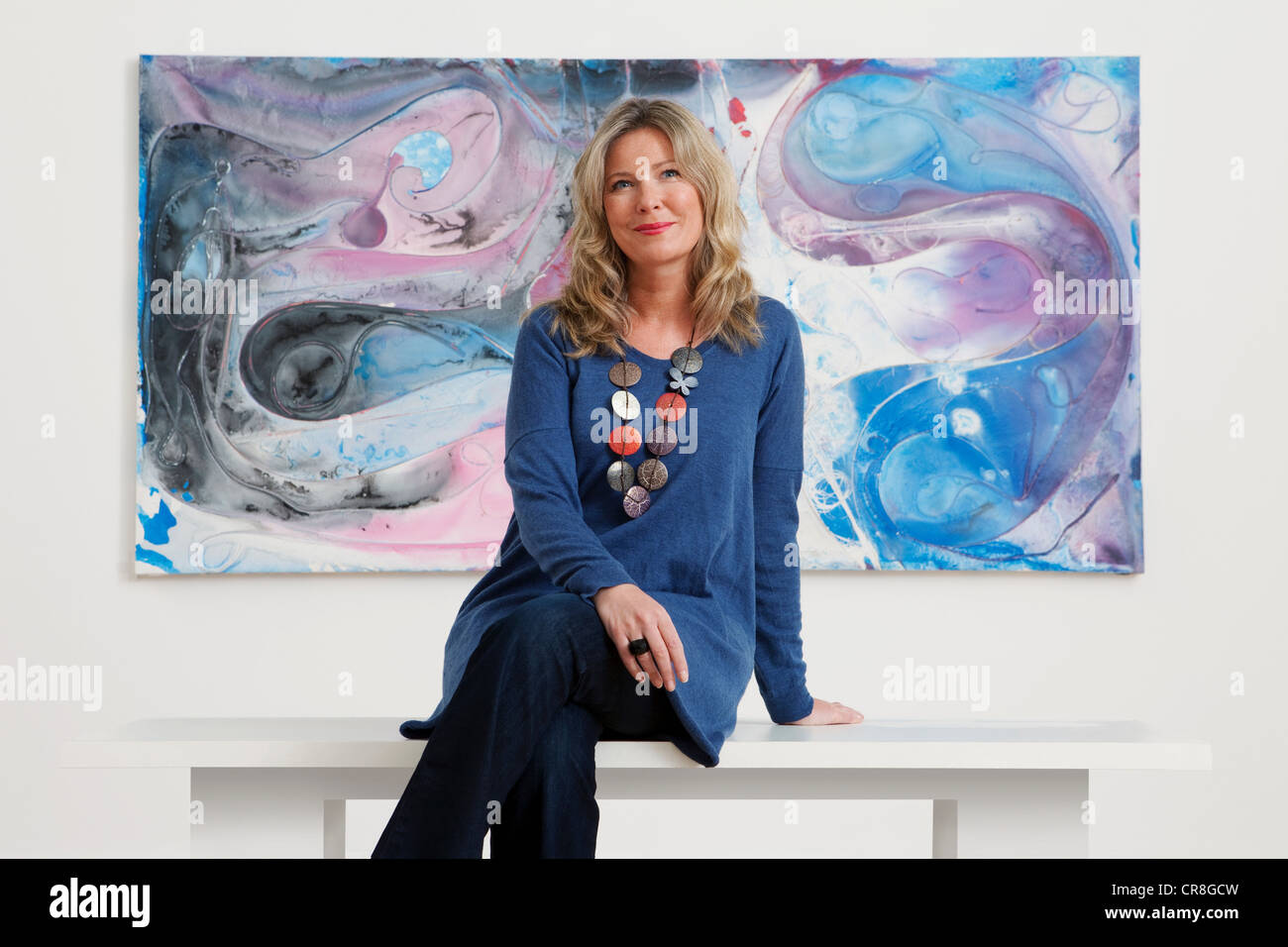 Mid adult woman sitting in front of oil painting in gallery Stock Photo