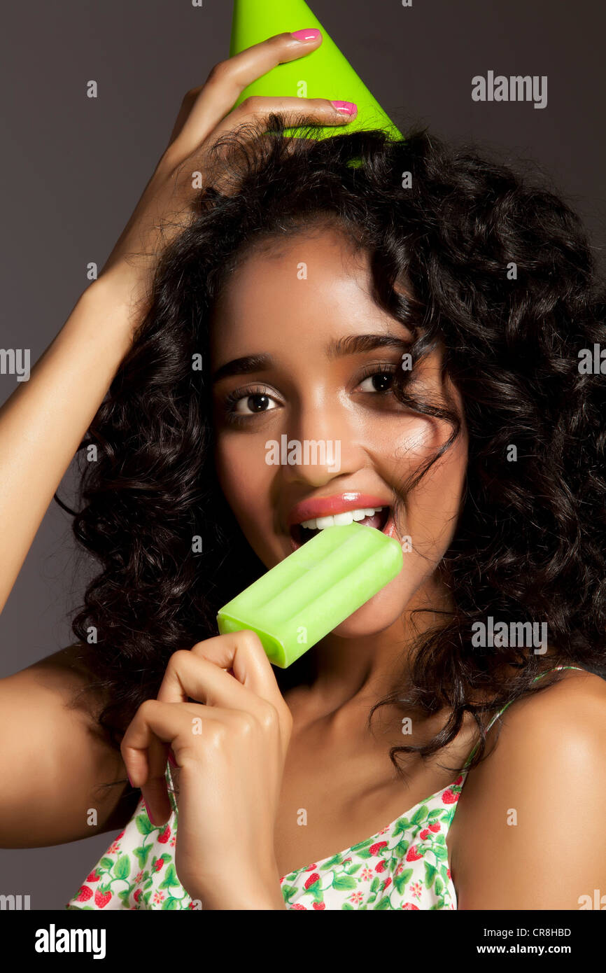Young woman eating green popsicle and wearing party hat, portrait Stock