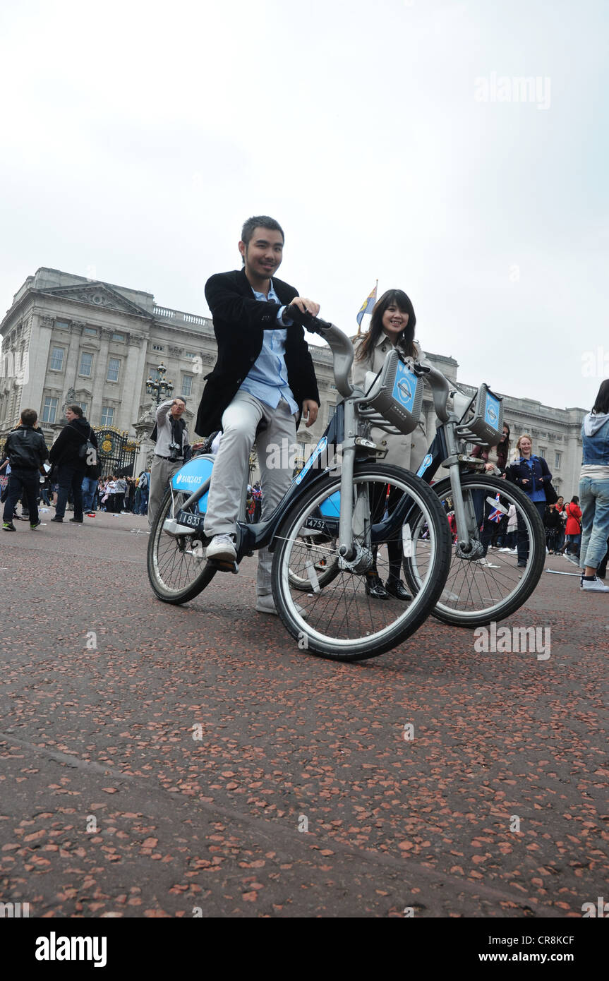 A couple posing on Boris bikes in front of Buckingham palace. Stock Photo