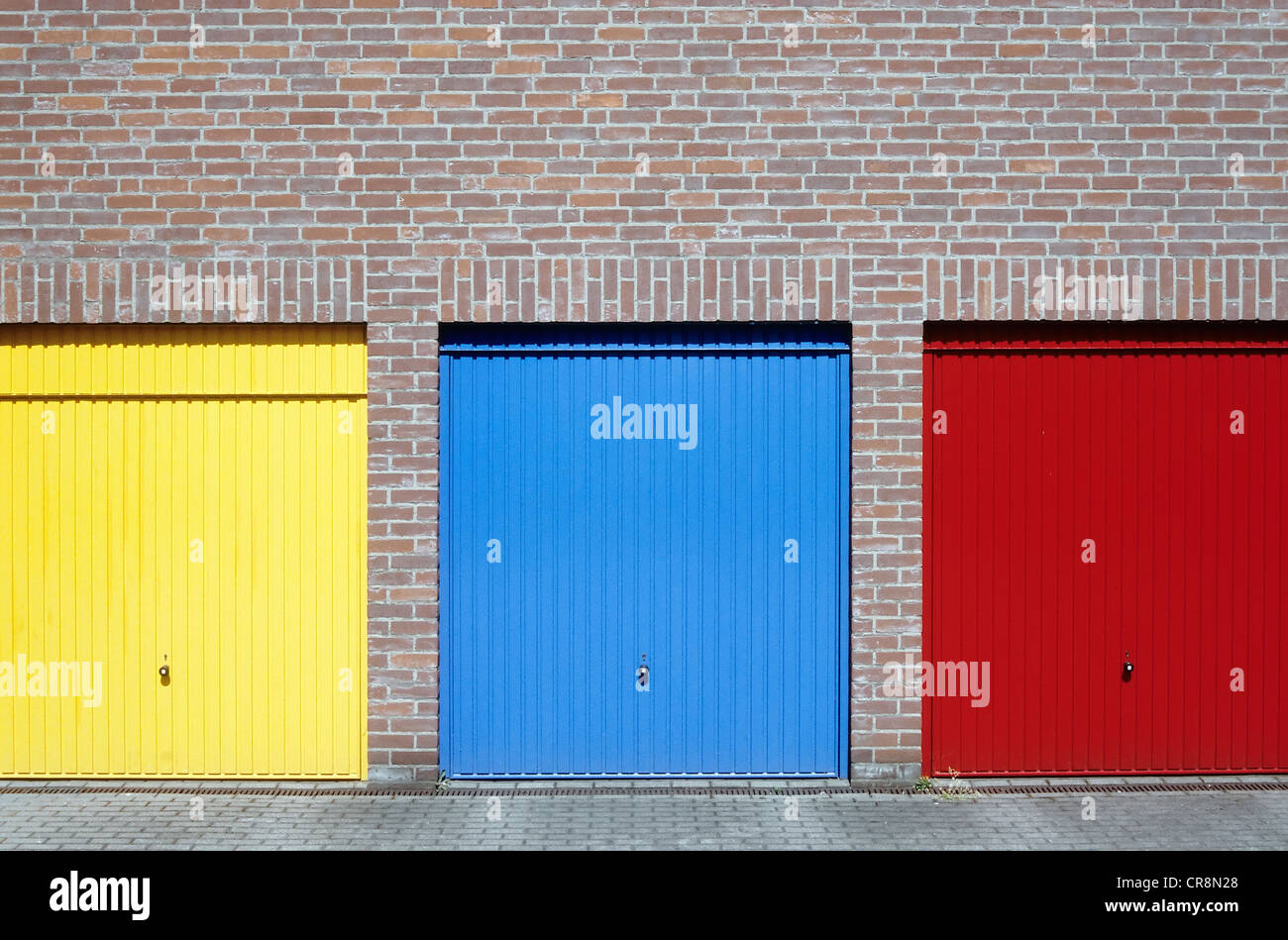 Three garage doors on a residential complex, painted in yellow, blue and red Stock Photo