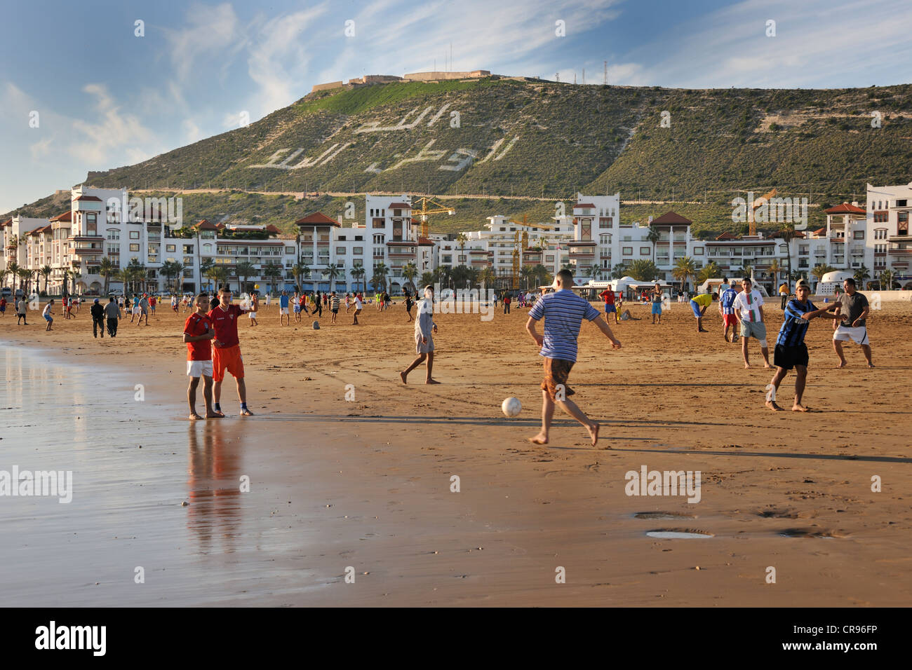 Playing football on Agadir Beach, hill with the words, Allah, al-Watan, al-Malik, meaning Allah, the Homeland, the King, Morocco Stock Photo