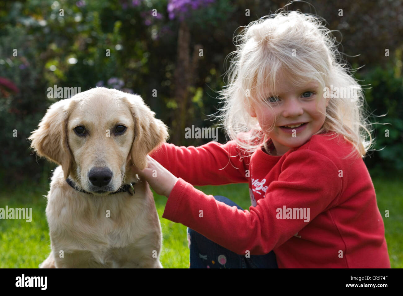 Blond girl sitting in a garden with a Golden Retriever, Upper Bavaria, Germany Stock Photo