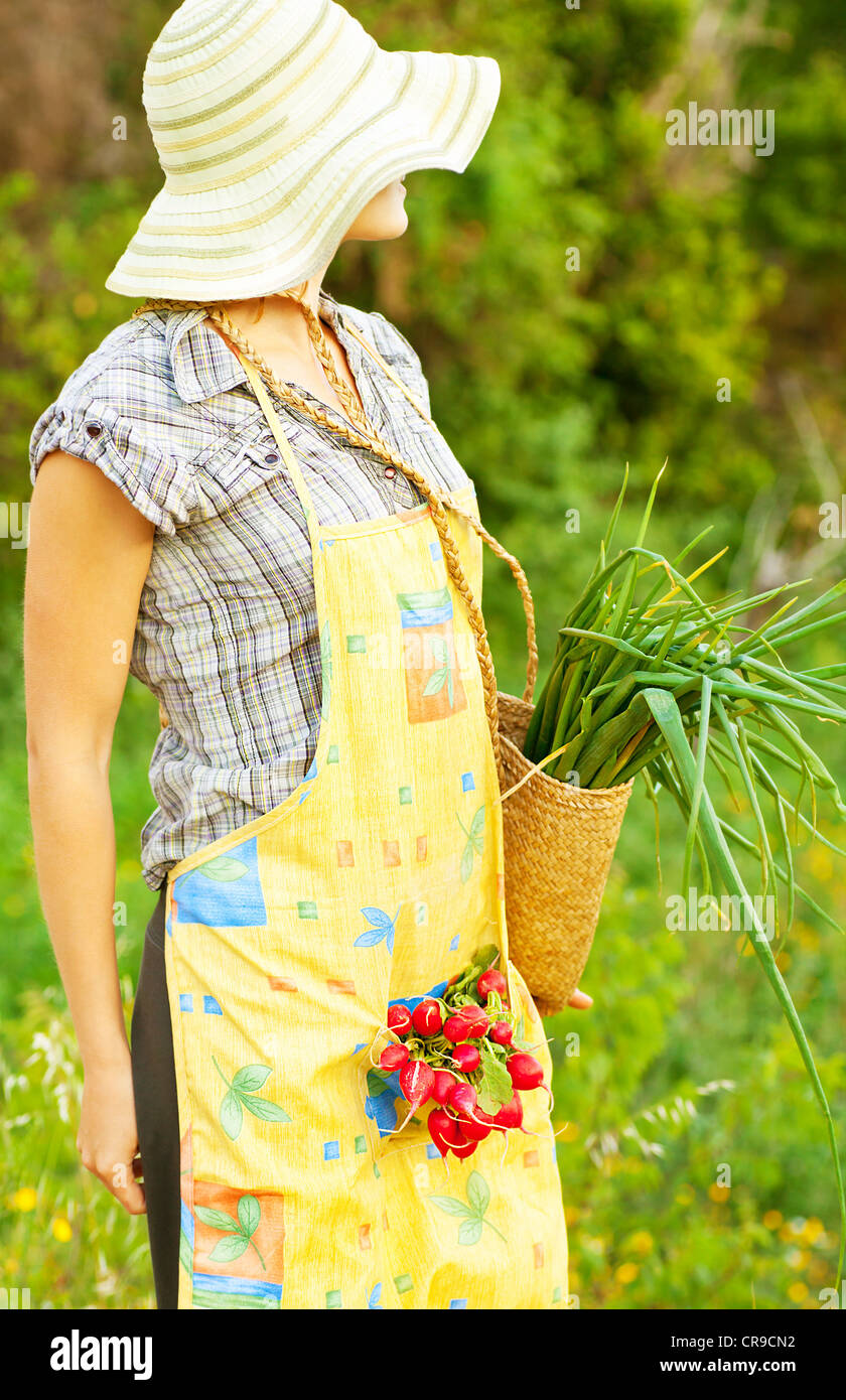 Happy woman gardener working on field, young female holding basket, girl growing organic green vegetables and fruits Stock Photo