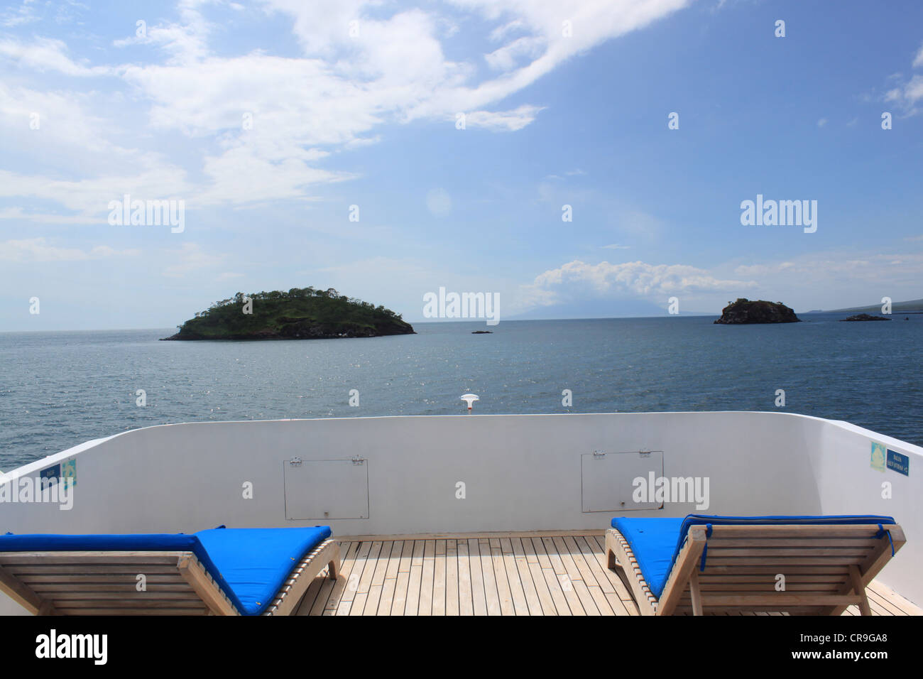 Two empty sun loungers on deck of boat overlooking two small islands Stock Photo