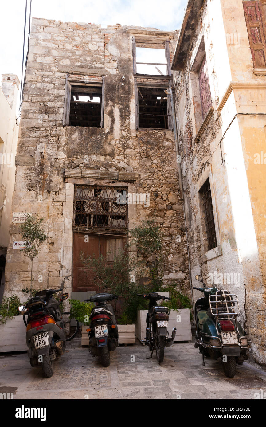 Mopeds parked in a tiny space in front of a semi-derelict building on a backstreet in Rethymnon, Crete Stock Photo