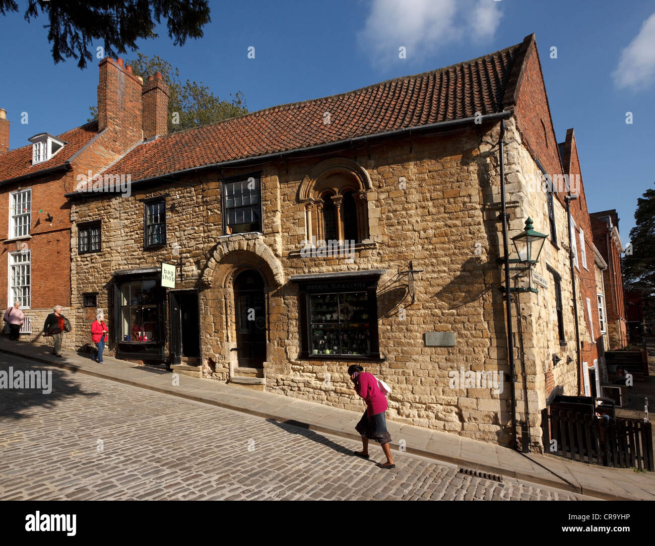 Woman struggles uphill past shops on old cobbled street, Steep Hill, Lincoln, Lincolnshire, England, UK Stock Photo