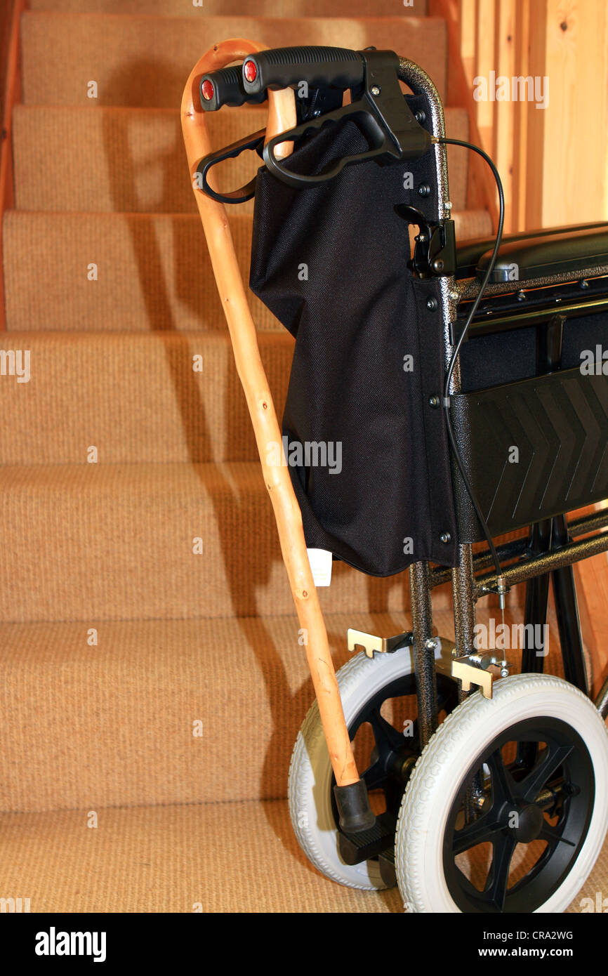 A wheelchair and walking stick by a staircase inside a house Stock