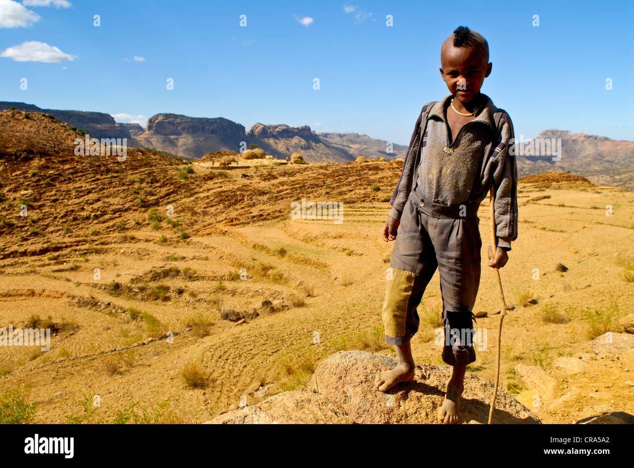 Black boy with a mohawk hairdo standing in front of the barren landscape of northern Ethiopia, Ethiopia, Africa Stock Photo