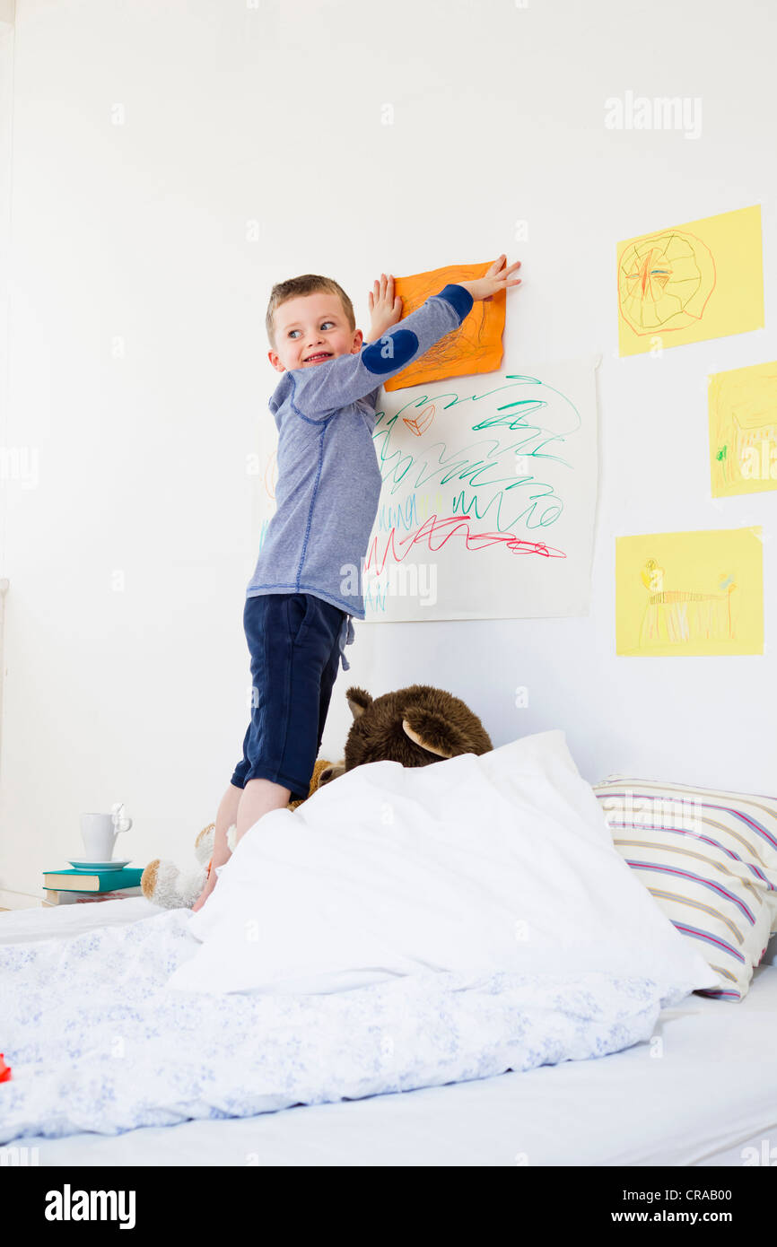 Boy hanging drawing on bedroom wall Stock Photo