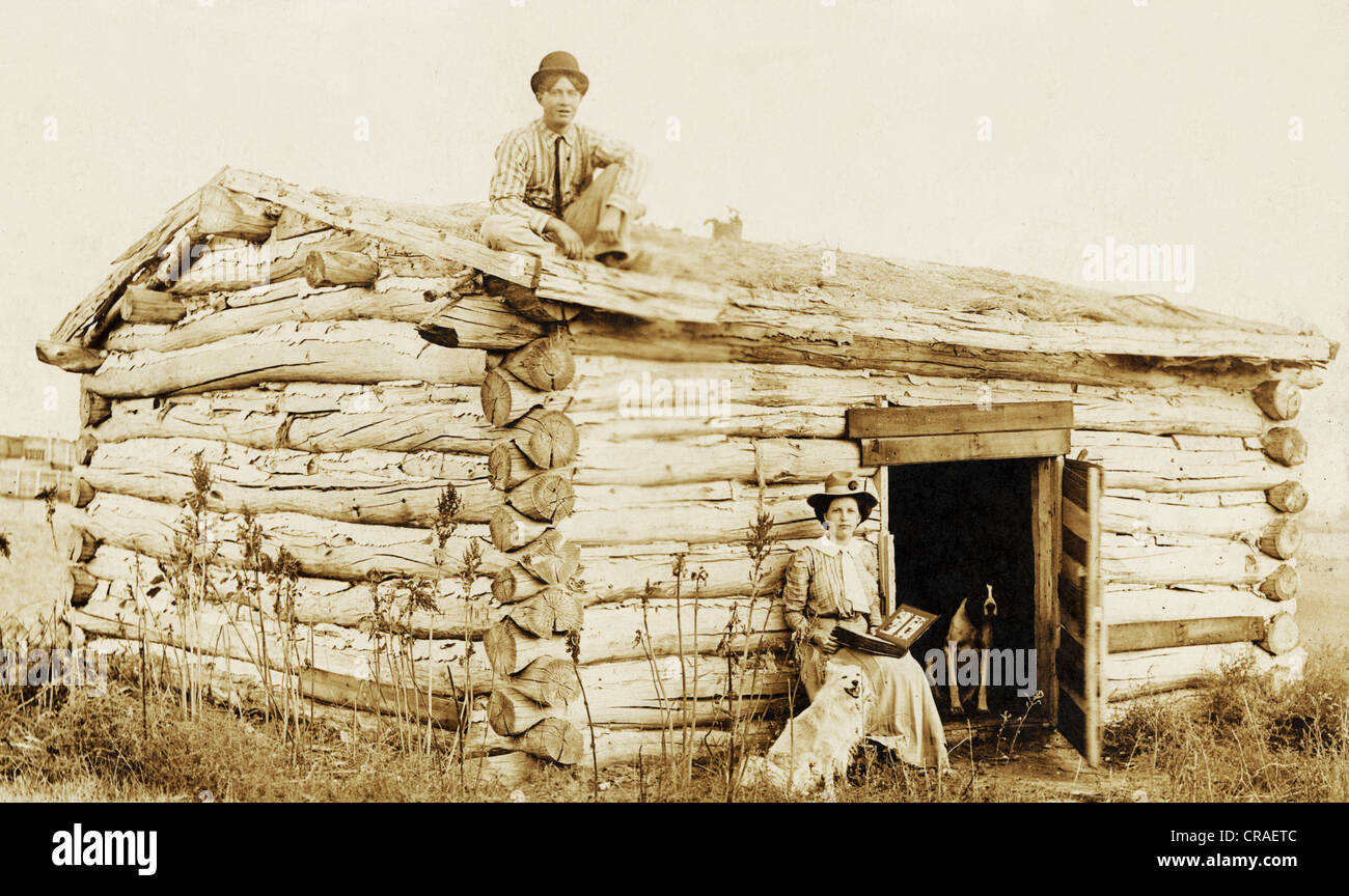 Young Man & Woman at Crude Windowless Log Cabin Stock Photo