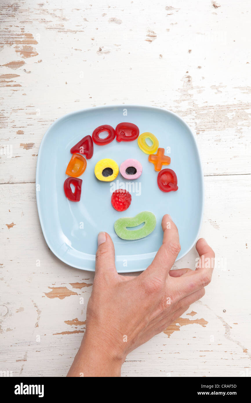 Hand reaching for candy, face made of gummy bears, food for children Stock Photo