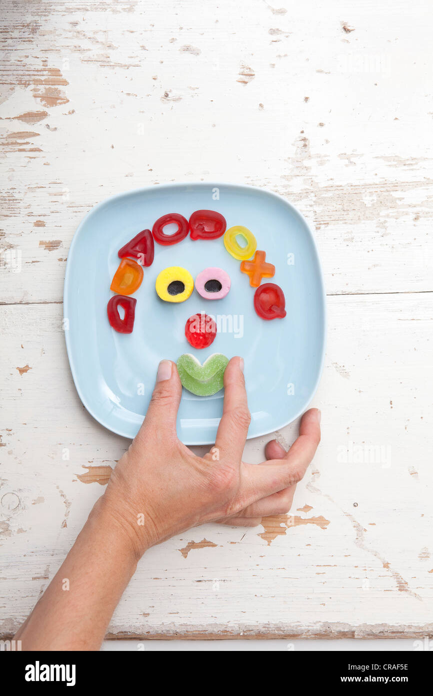 Hand forming a smiling mouth, face made of gummy bears, food for children Stock Photo