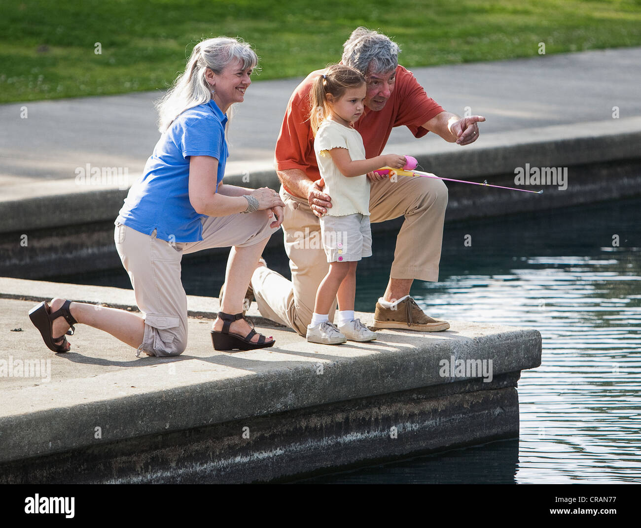 Grandparents fish with their granddaughter at local pond. Stock Photo
