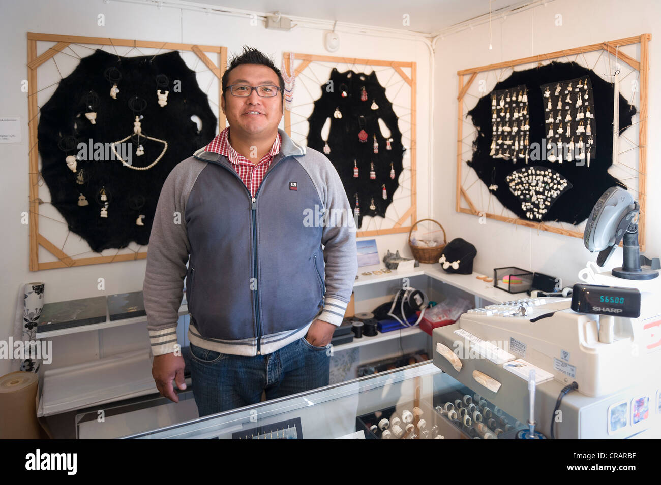 Inuit man standing in front of a jewellery display in the souvenir shop of the tourist office, Tasiilaq or Ammassalik Stock Photo