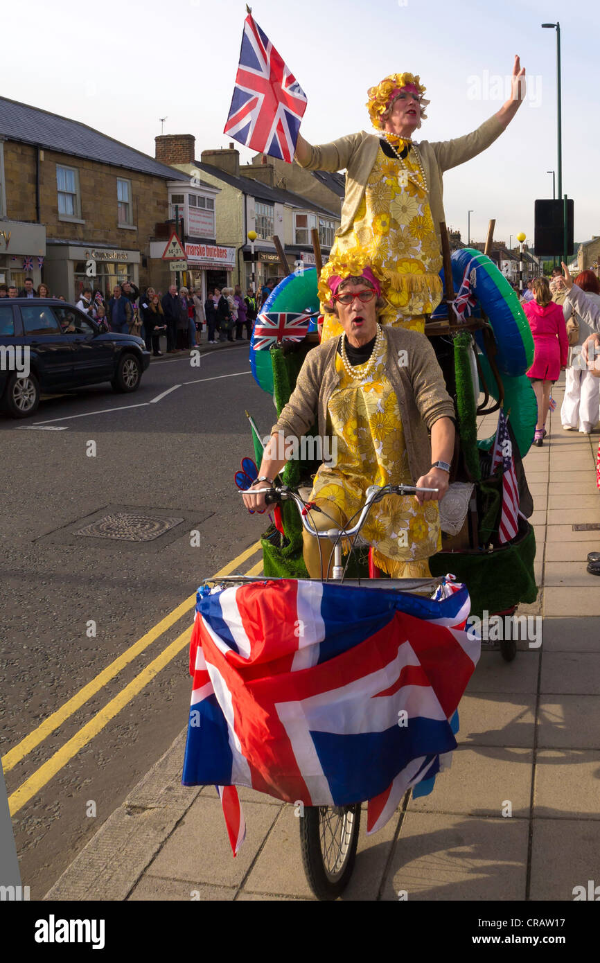 Women in fancy dress riding tandem tricycle sing singing decorated Union flag flags Jack Jacks Olympic Torch relay June 18 2012 Stock Photo