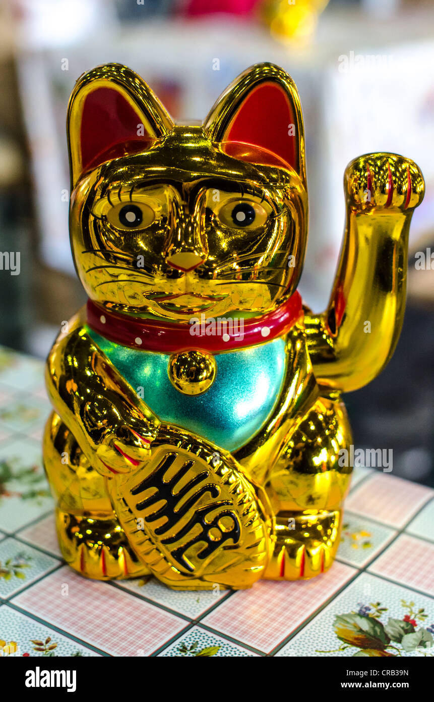 Golden, shiny plastic waving cat ('lucky cat') on table with tablecloth. Stock Photo