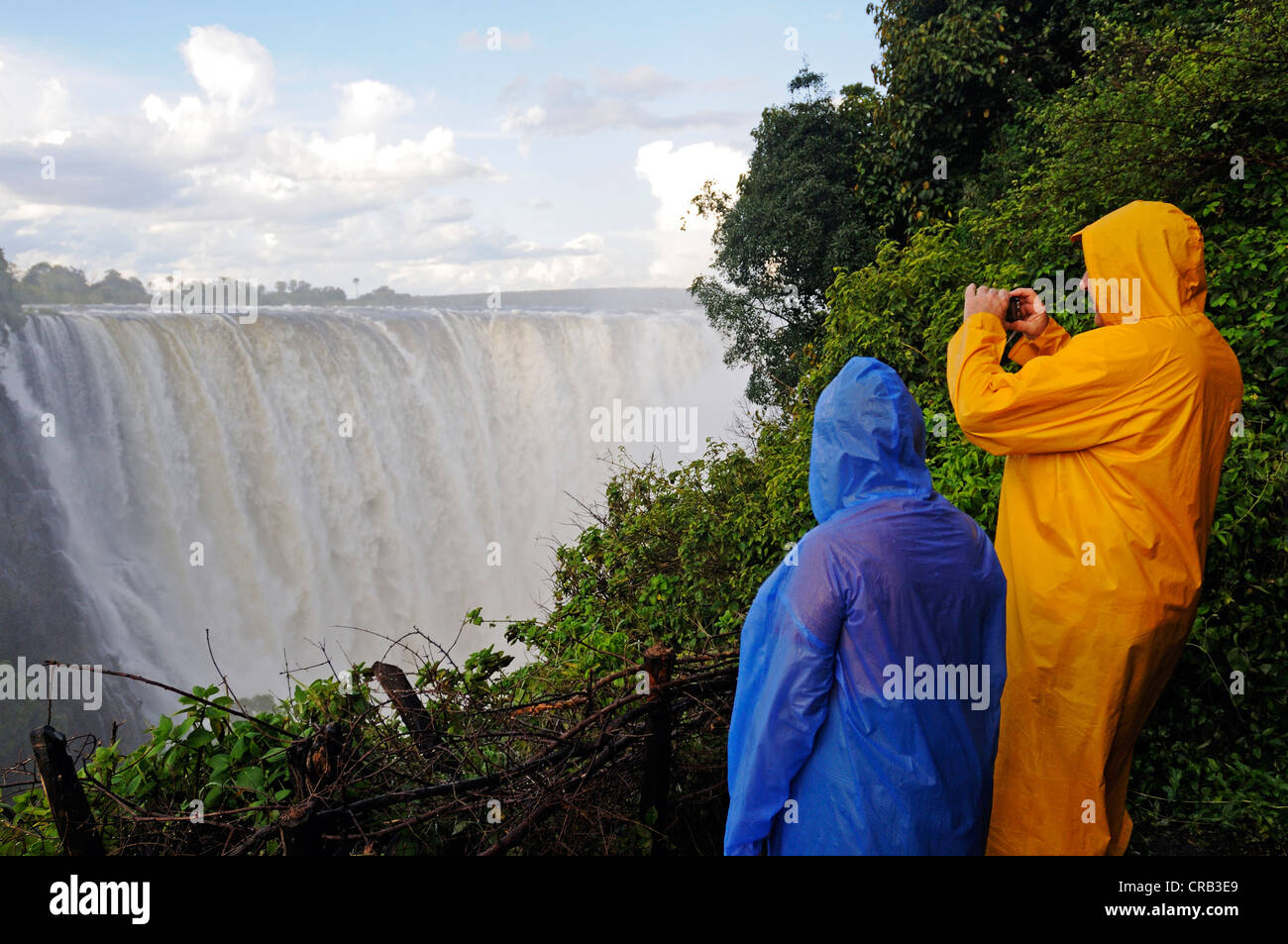 Tourists in rain jackets photographing the Victoria Falls, waterfall on the Zimbabwean side of the river Zambezi Stock Photo