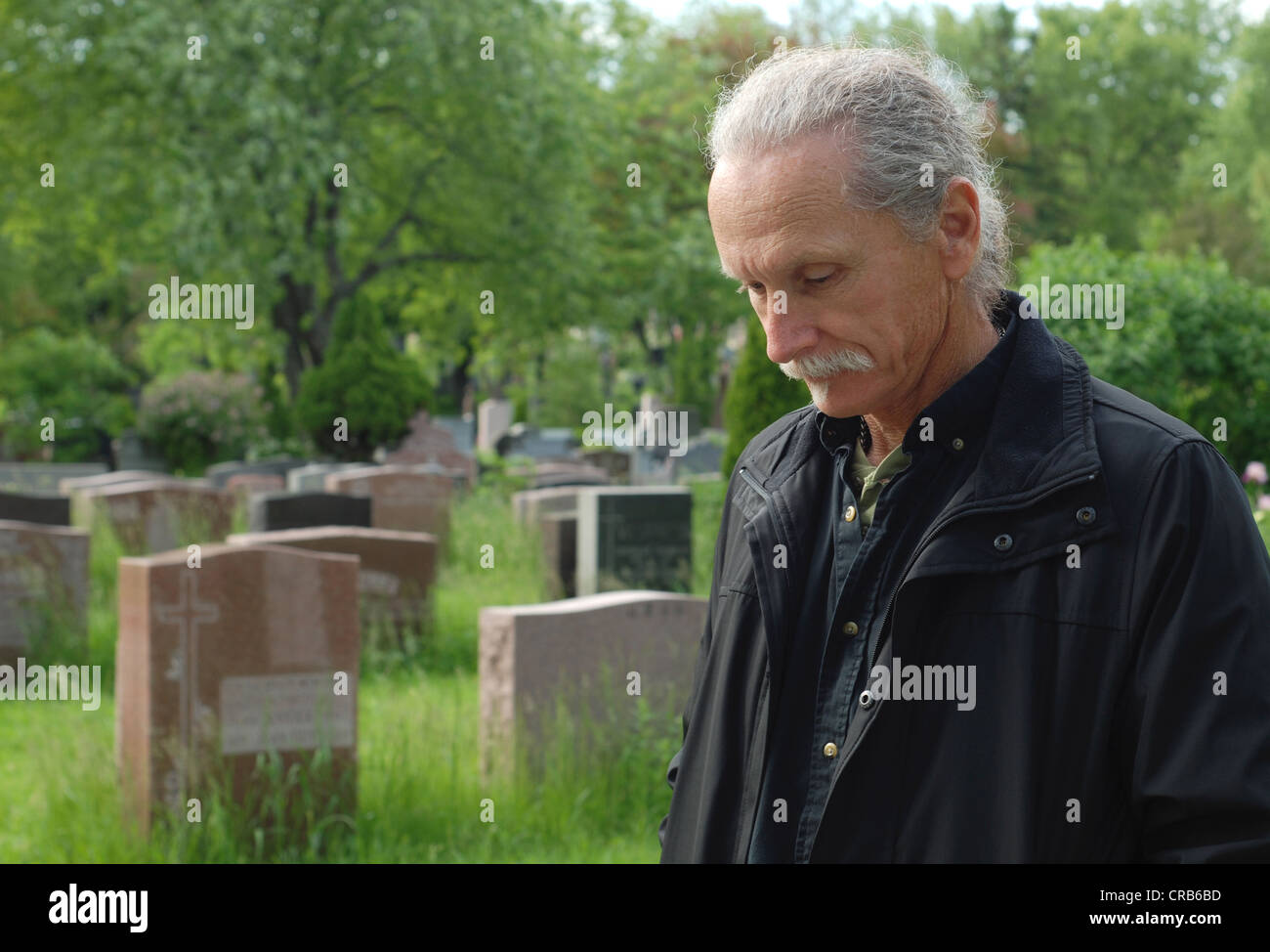Sorrowful man standing in cemetery with head bowed Stock Photo