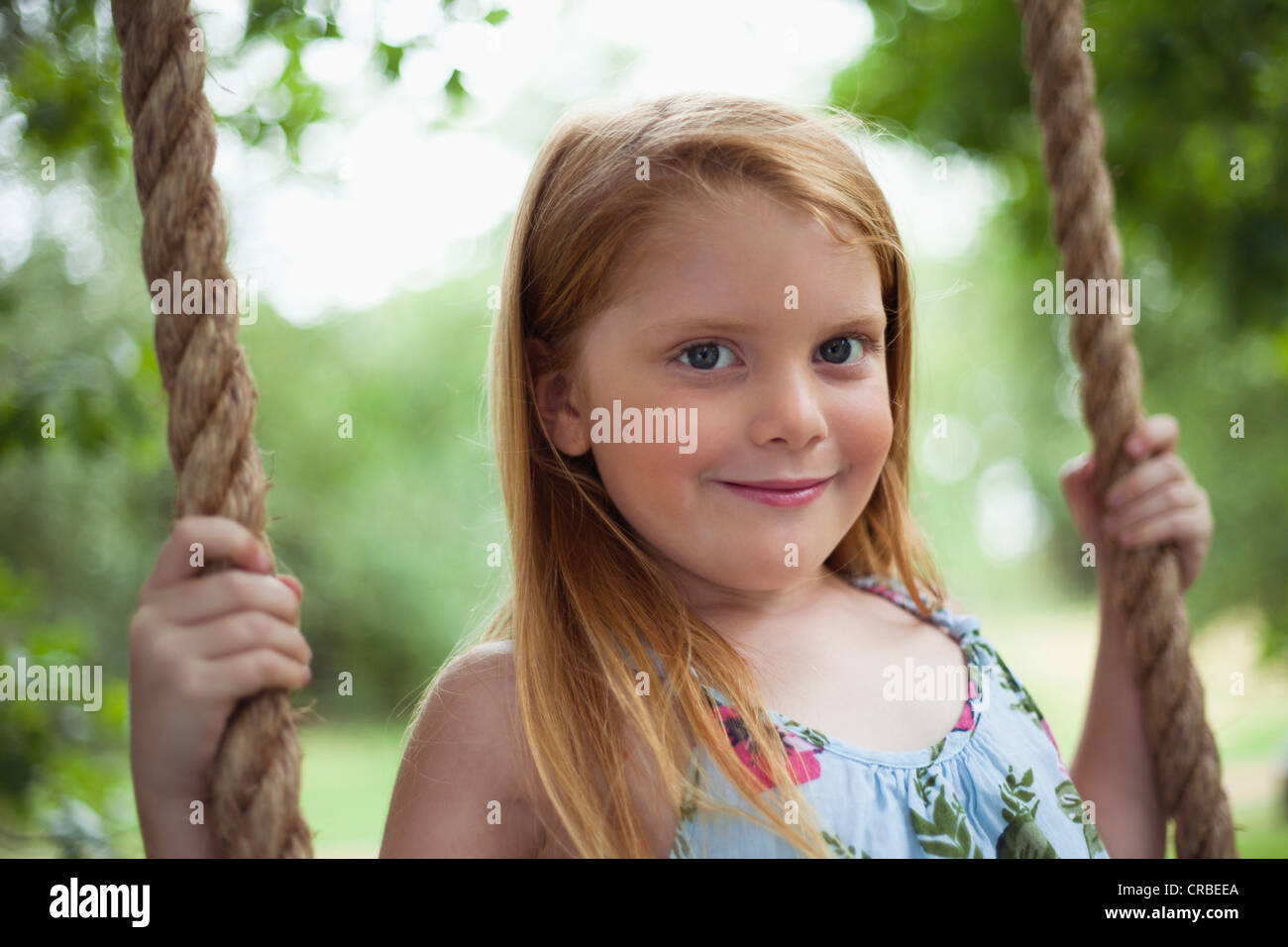 Smiling girl sitting in tree swing Stock Photo