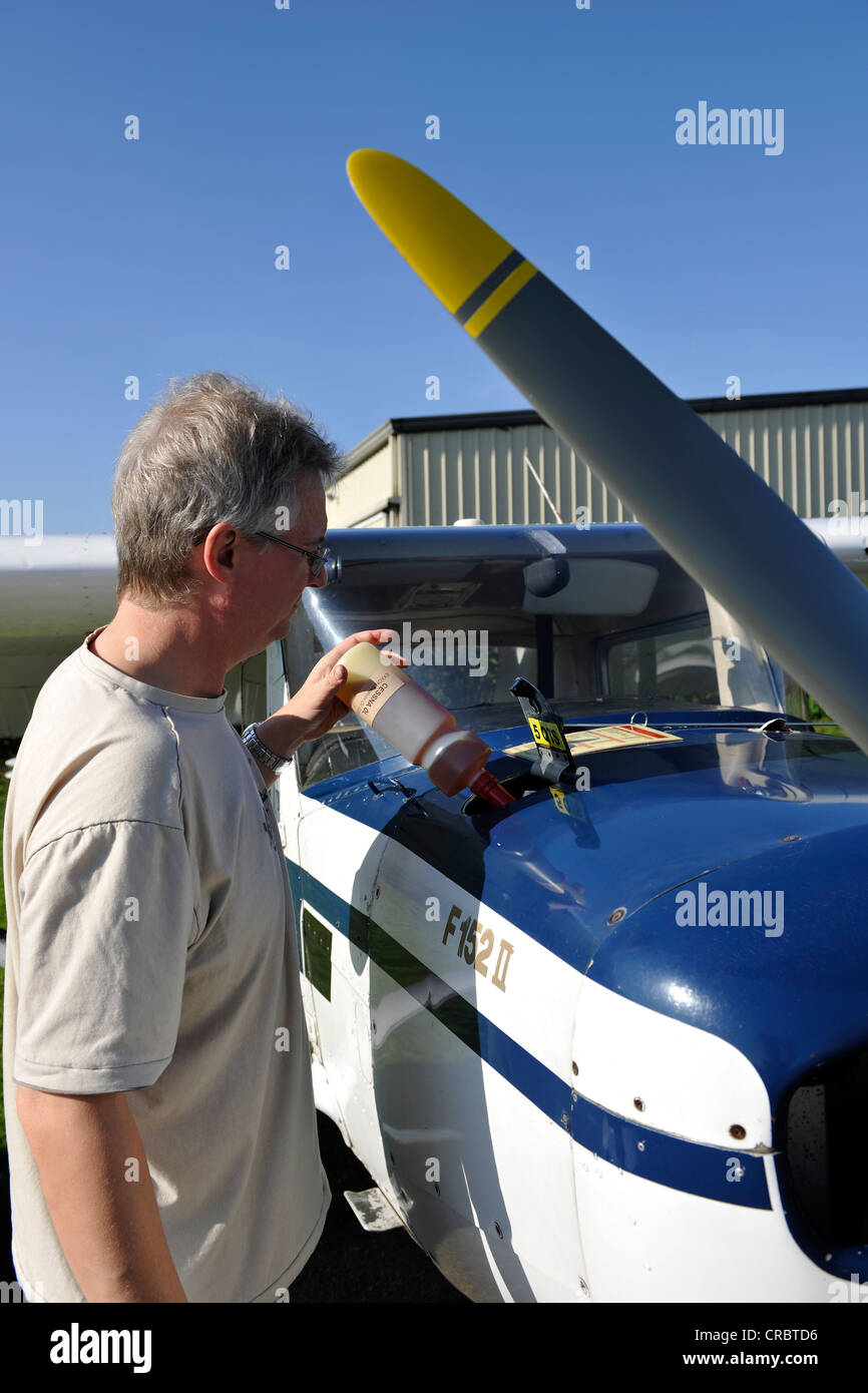 Pilot topping up engine oil of a Cessna 152 before a flight, Airport