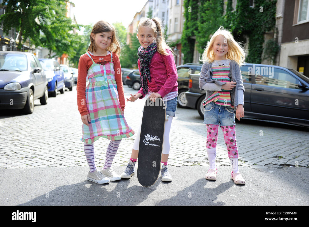 Three girls with a skateboard in a residential street in the centre of Dusseldorf, North Rhine-Westphalia, Germany, Europe Stock Photo