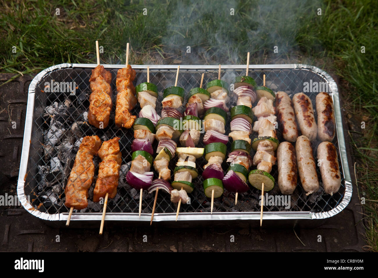 Disposable charcoal barbecue cooking kebabs and sausages Stock Photo