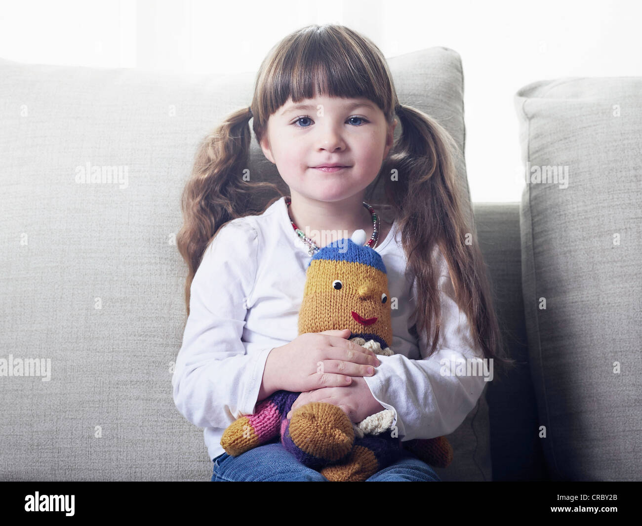 Girl hugging stuffed animal on sofa Stock Photo