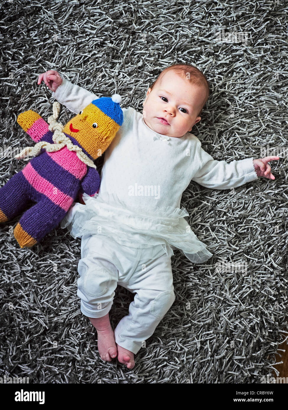 Baby laying on rug with stuffed animal Stock Photo