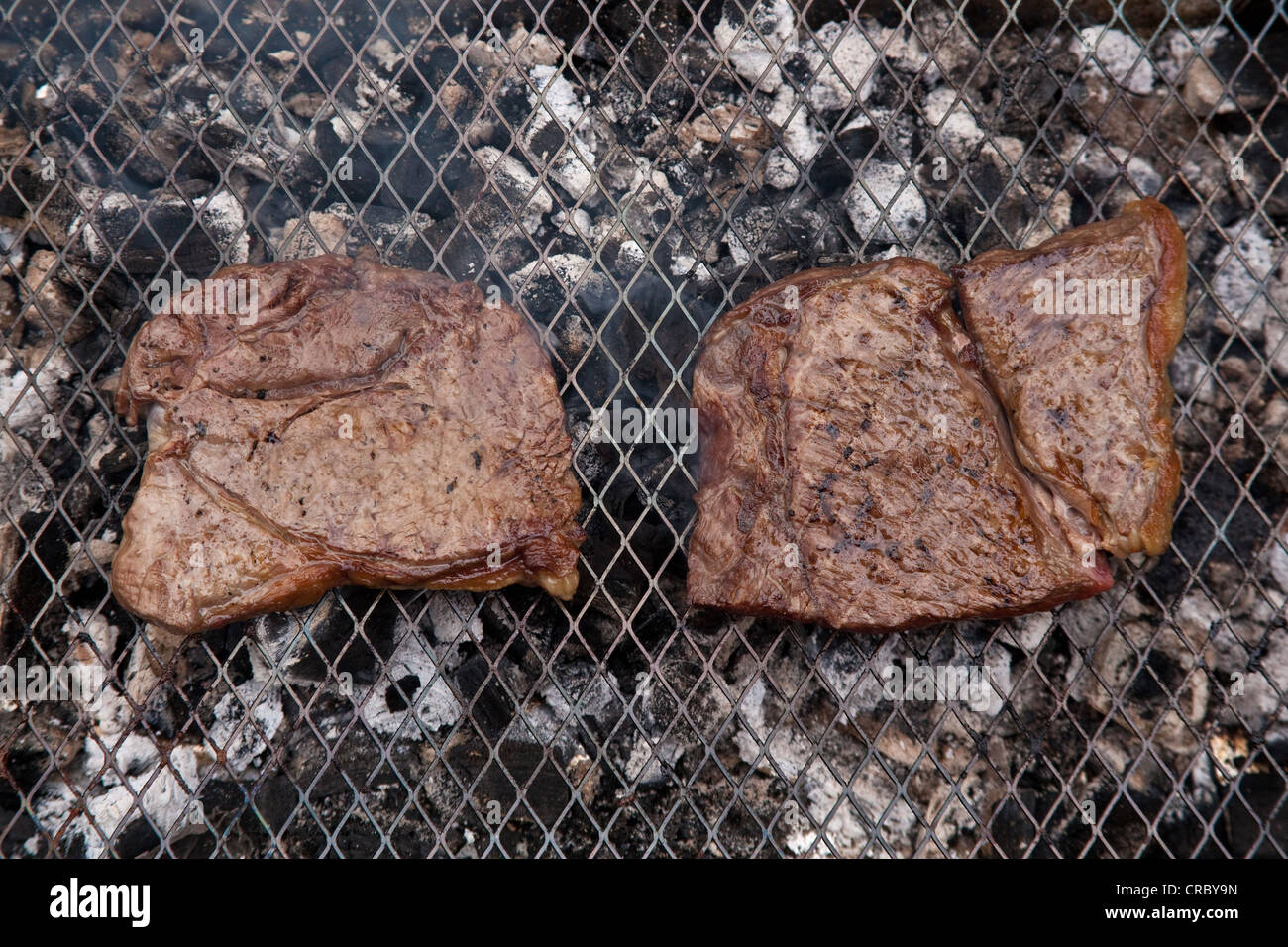 Rump steak cooking on a charcoal barbecue. Stock Photo