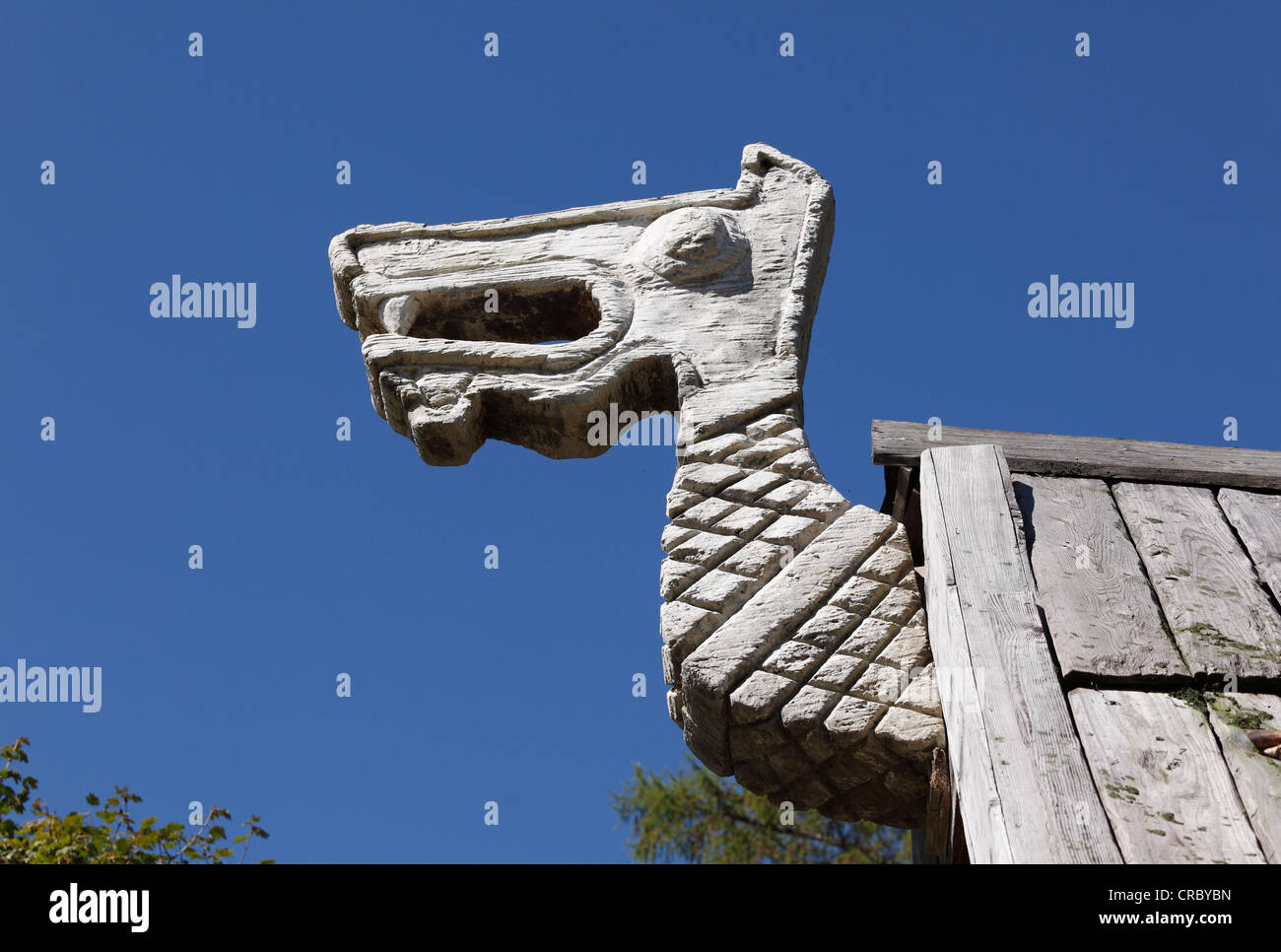 Head of a dragon, decoration on a wooden hut at the Flake Viking village on Lake Walchen, Herzogstand mountain at the back Stock Photo