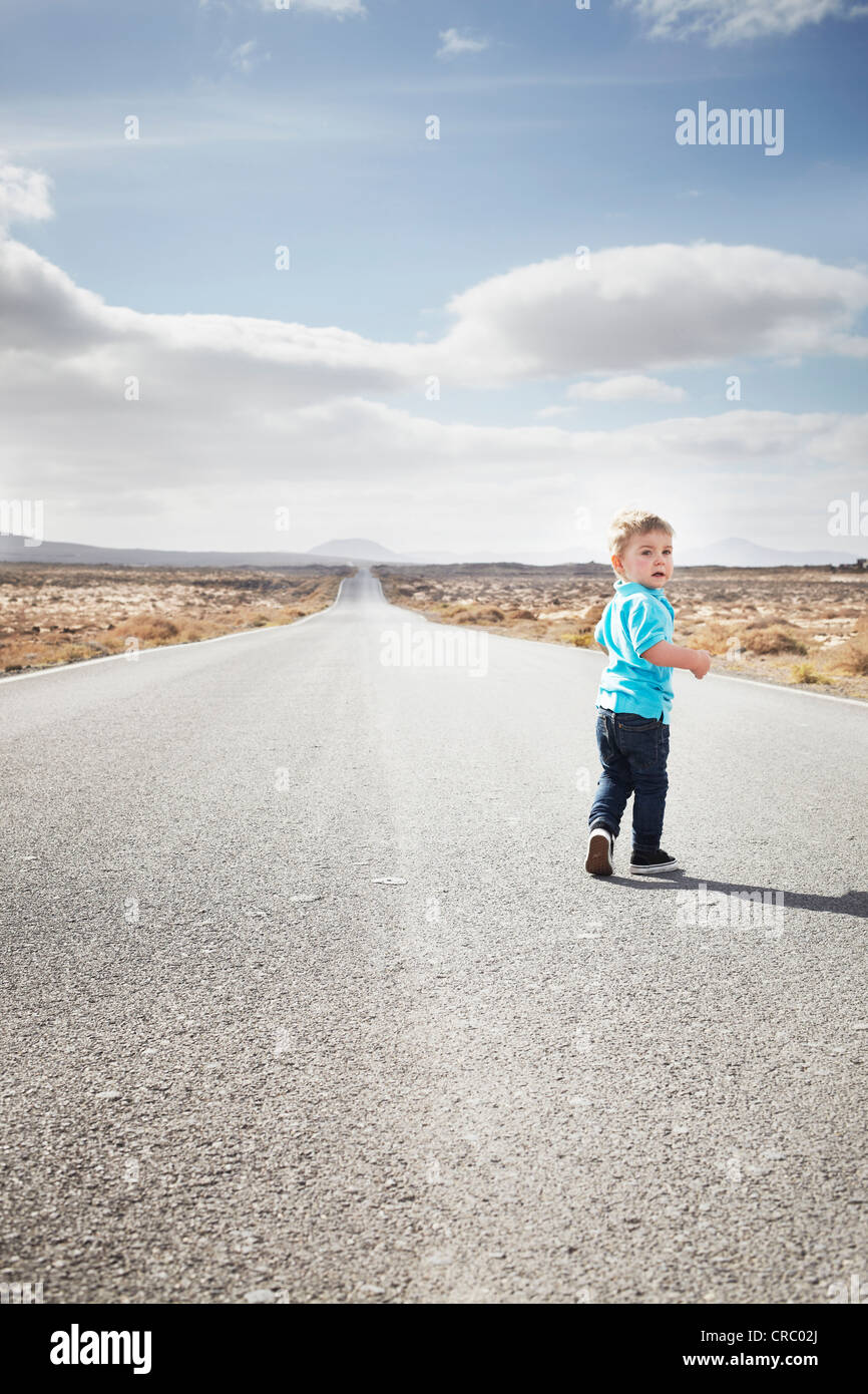 Boy walking on paved rural road Stock Photo