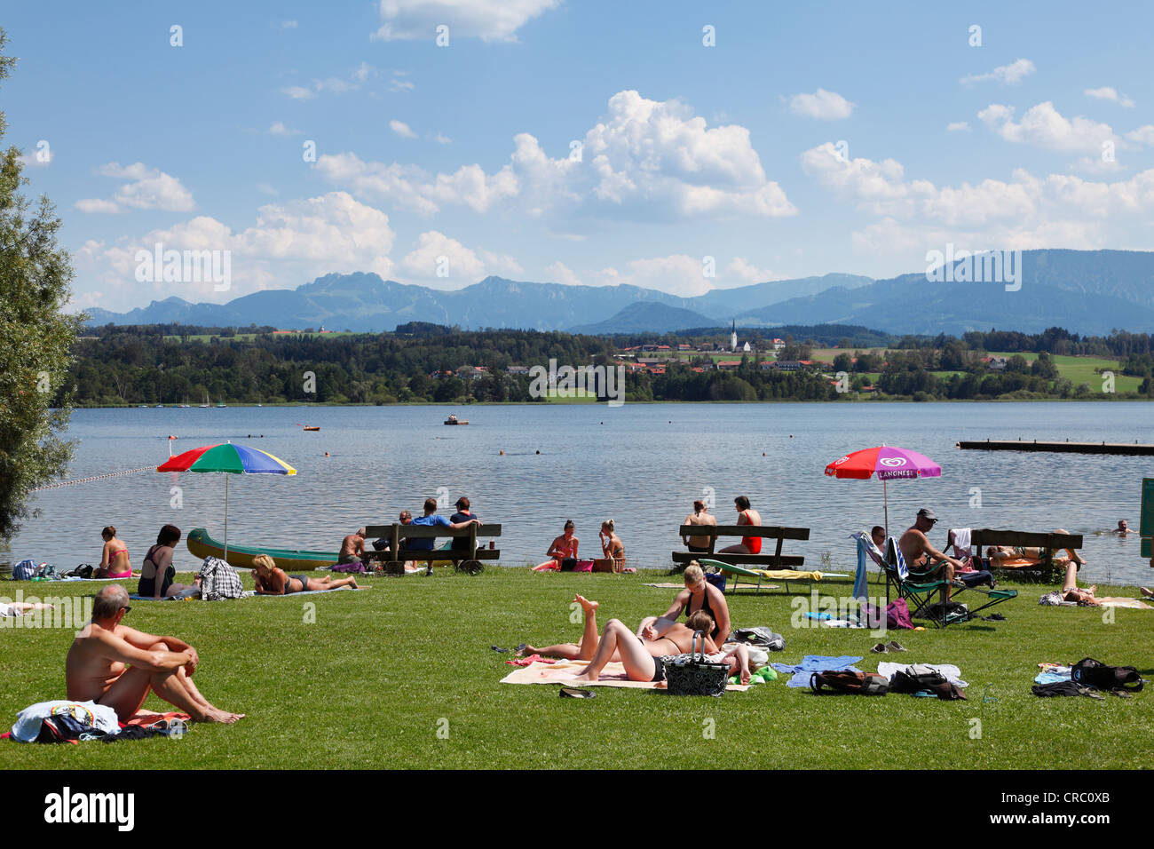Holidaymakers sunbathing at Simssee lake near Stephanskirchen, Neukirchen at back, Chiemgau, Upper Bavaria, Bavaria Stock Photo