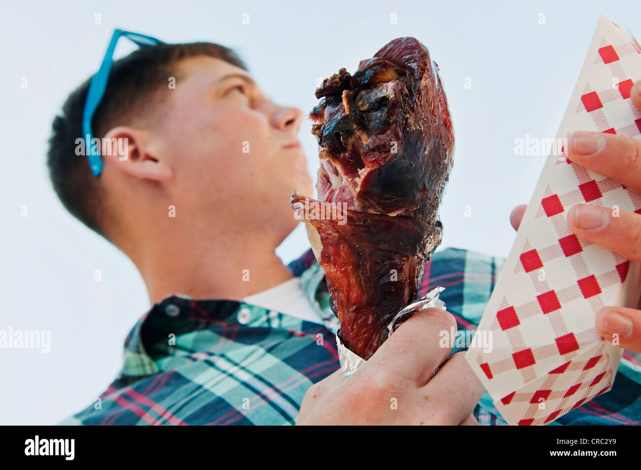 Closeup of theme park giant barbecued turkey drumstick held by a young adult male. Stock Photo