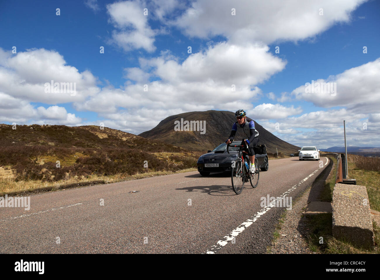cyclist being overtaken by car on rural country road the a82 road in glencoe highlands scotland uk Stock Photo