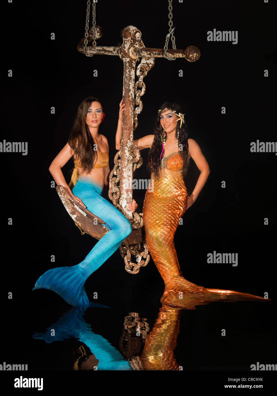 Two young mermaids sitting on a large anchor hanging above a reflection pool. Stock Photo