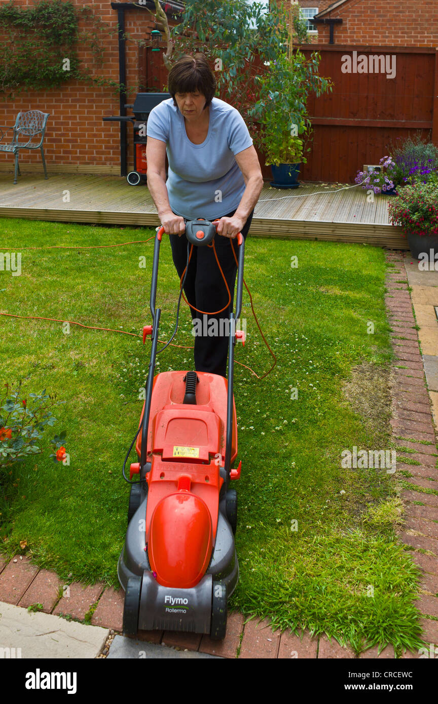 Mature woman mowing the lawn with an electric mower Stock Photo