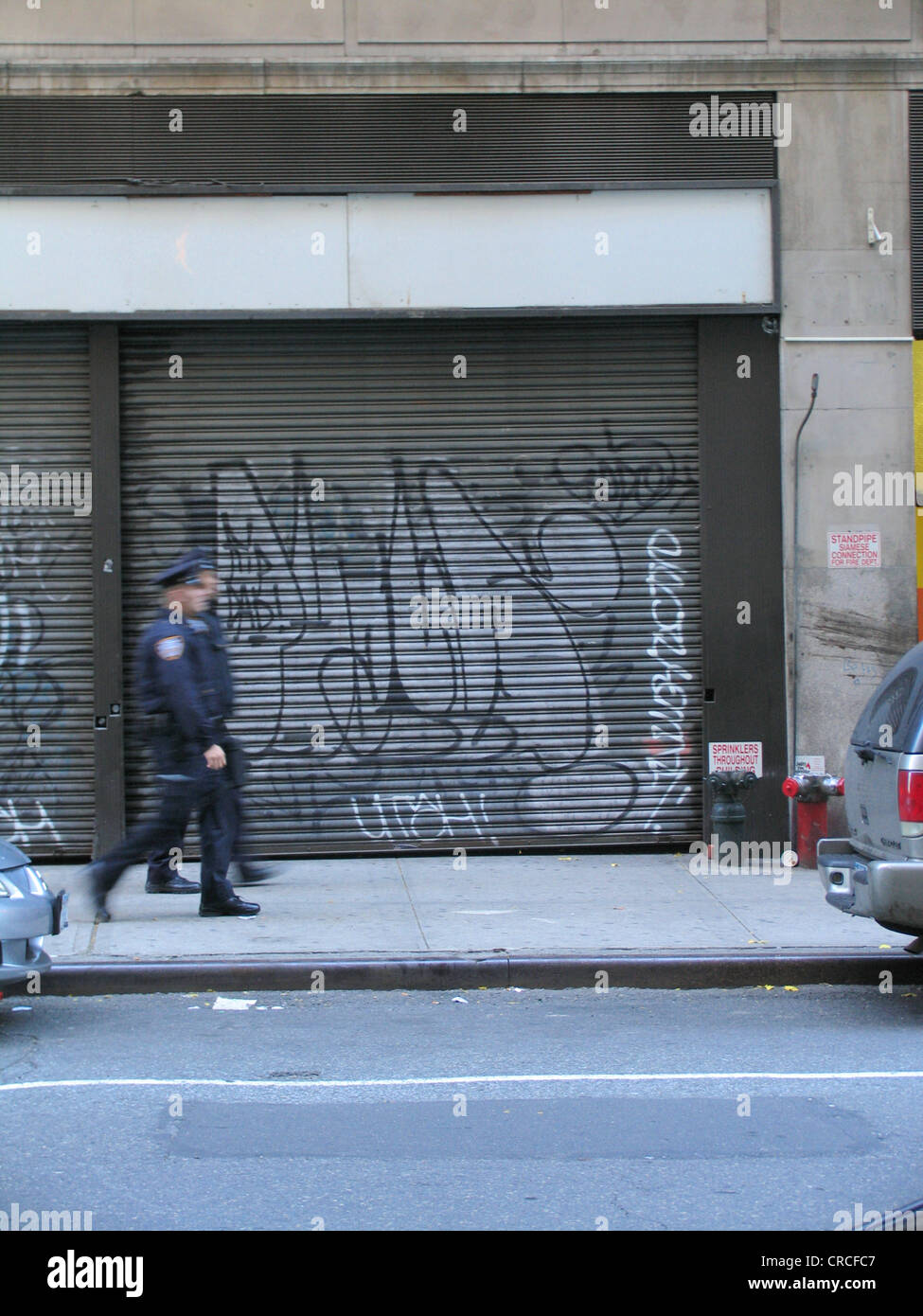 policemen walking in front of metal shutters with graffiti, USA, Manhattan, New York Stock Photo