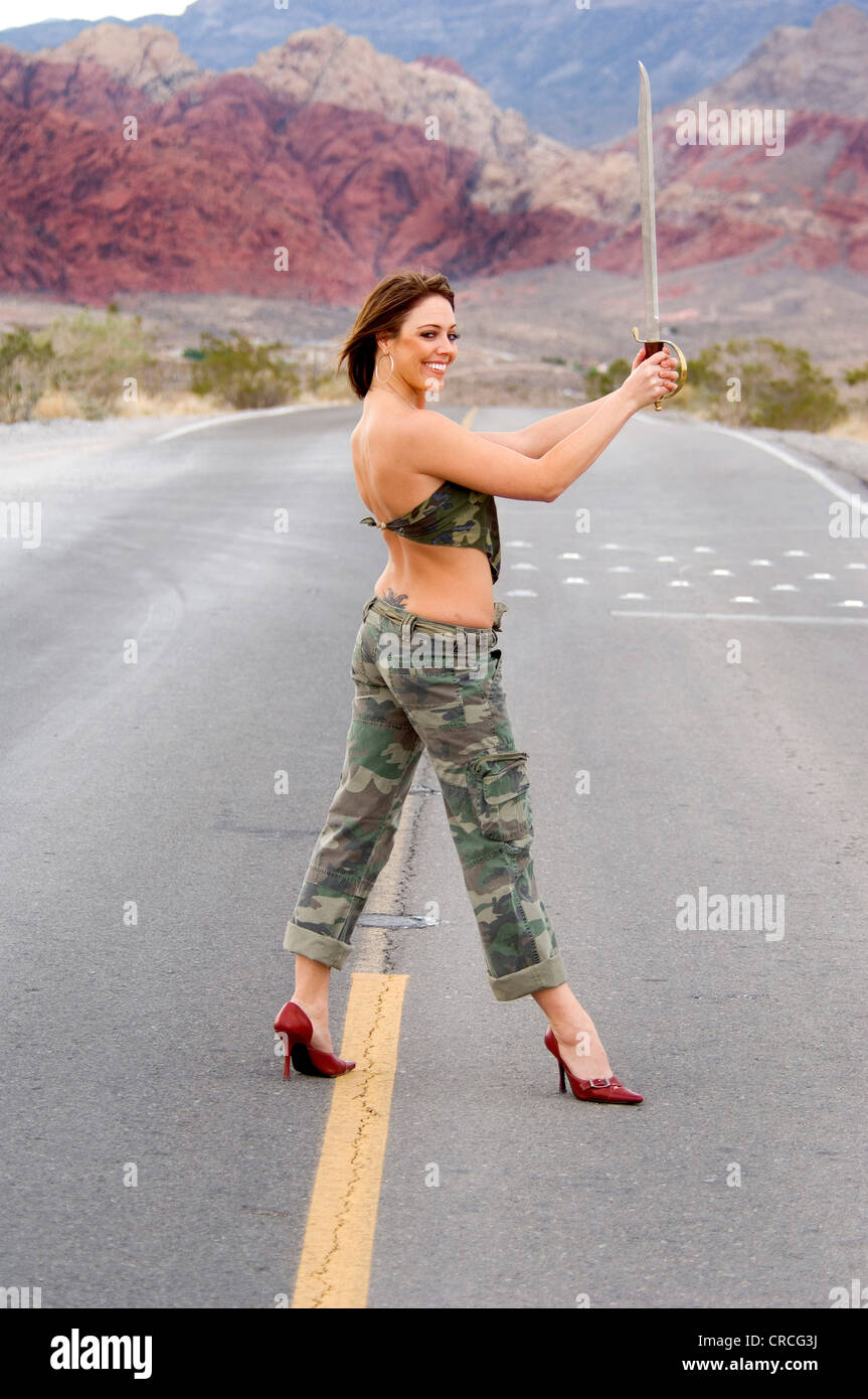 woman with a sword in fatigues on country road in the desert Stock Photo