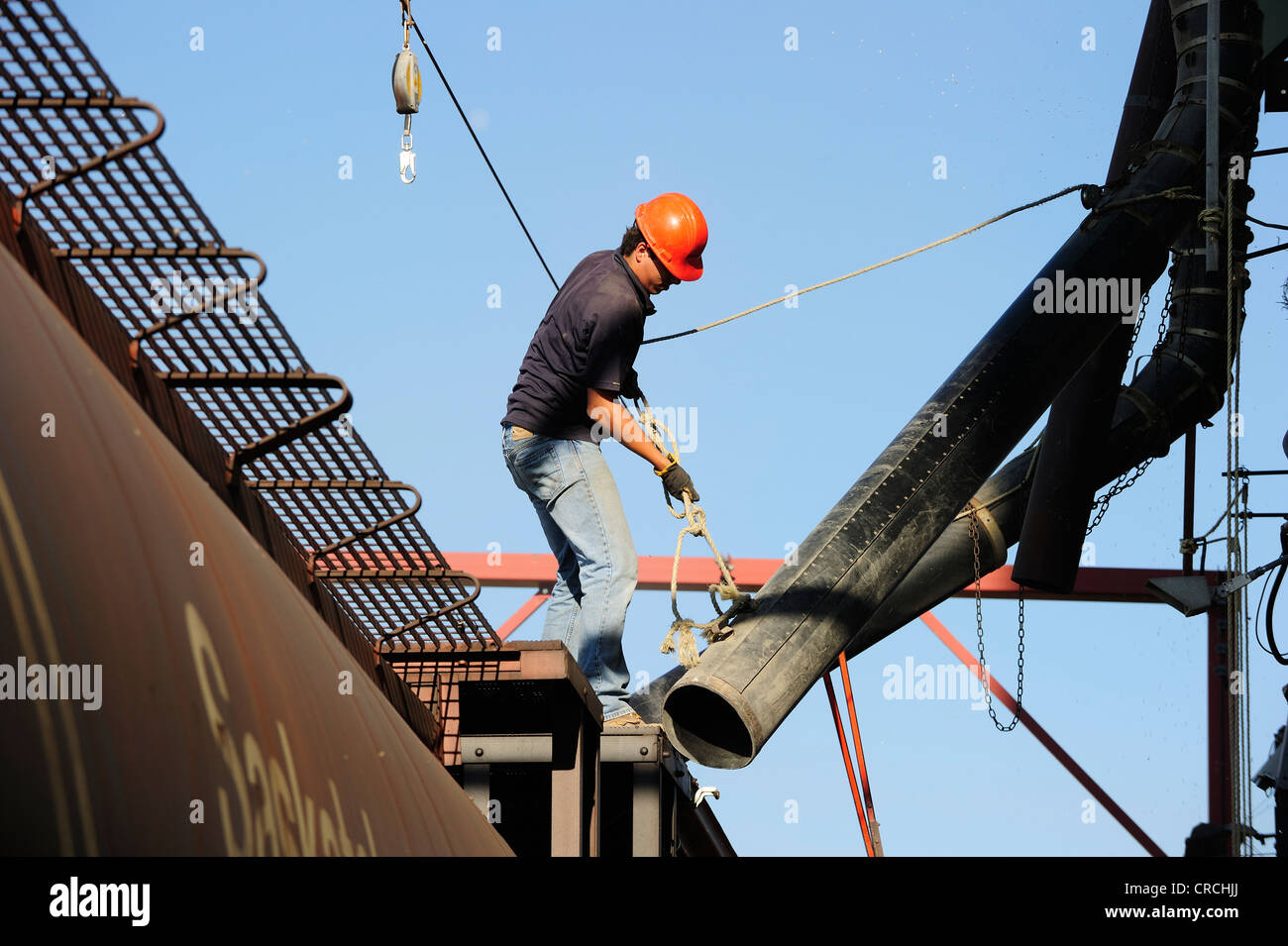 Worker on a train moving the filler hose of the grain silo to the train's opening to fill it with grain, Saskatchewan, Canada Stock Photo