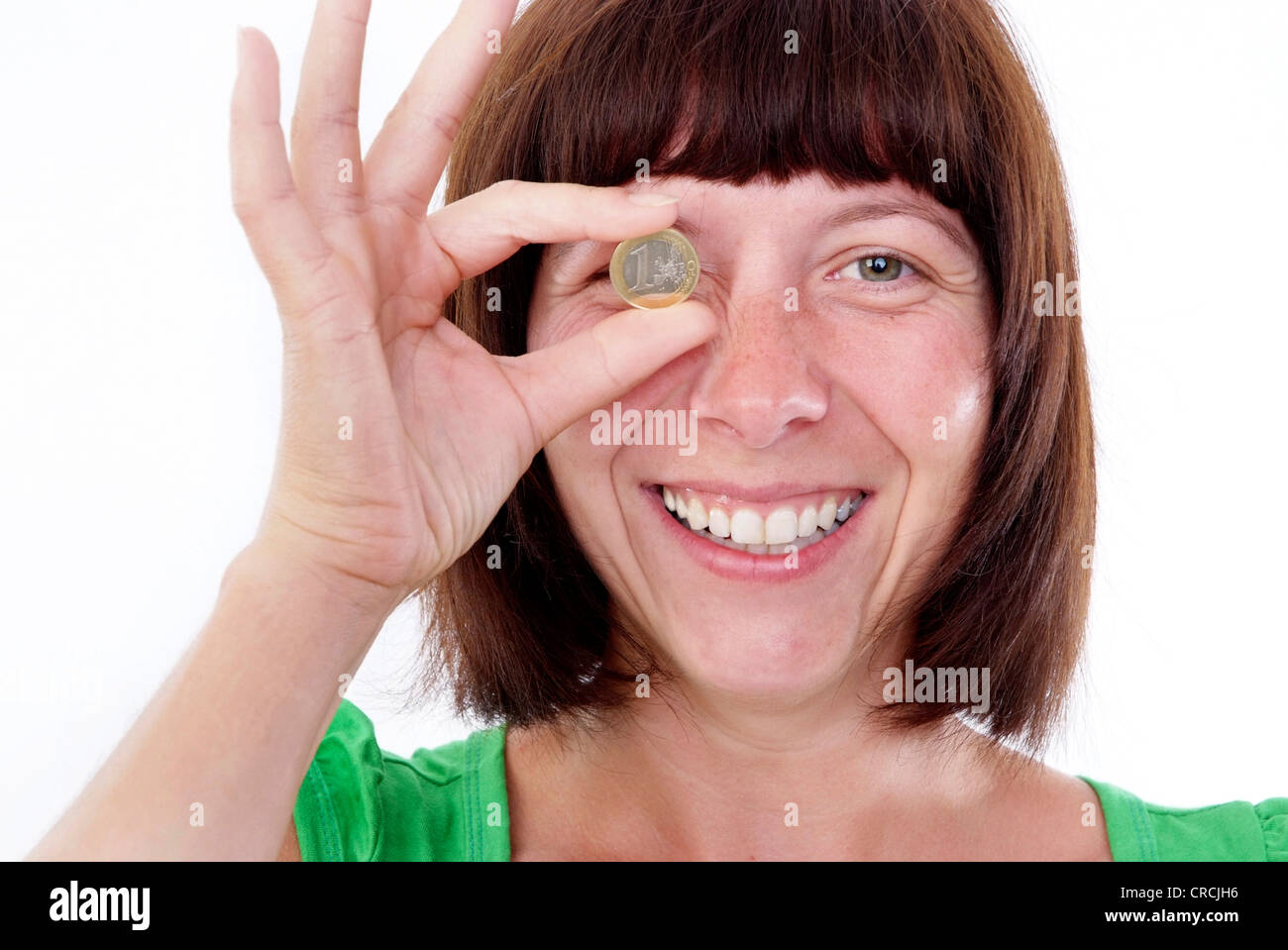 brown-haired woman holding an Euro coin in front of her eye Stock Photo