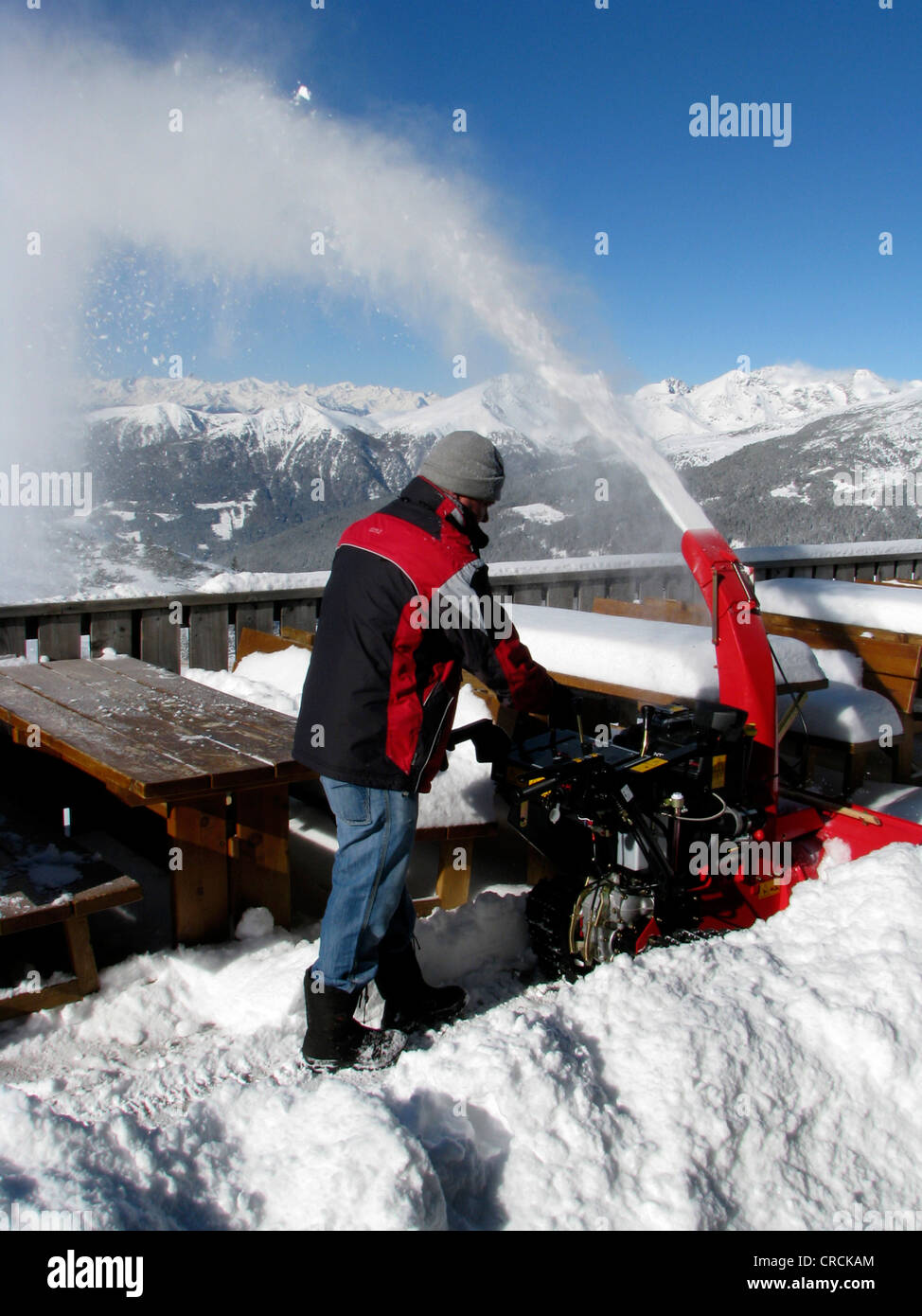 Man cleaning off fresh snowfall with a machine off a terrace of a restaurant in a skiing area, Italy, Suedtirol, Sarntal, Sarentino, Reinswald Stock Photo
