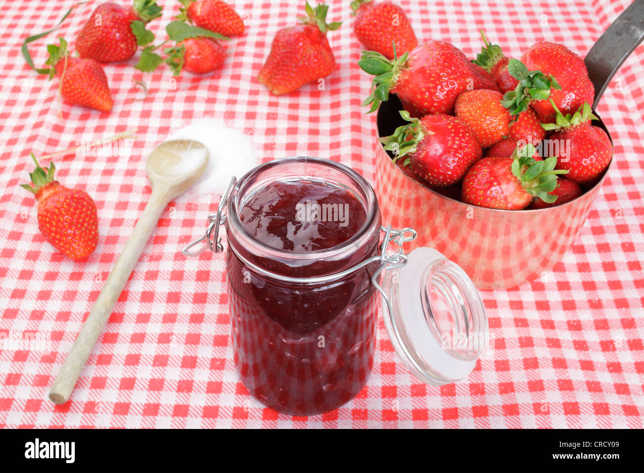 Strawberry jam in a glass, strawberries in a copper pot and sugar on a wooden spoon Stock Photo