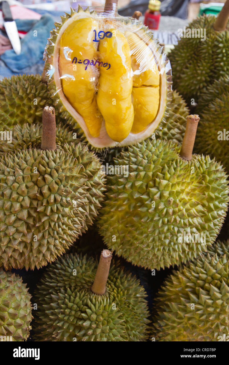 Durian for sale on a market stall with open fruit covered with plastic wrap Stock Photo