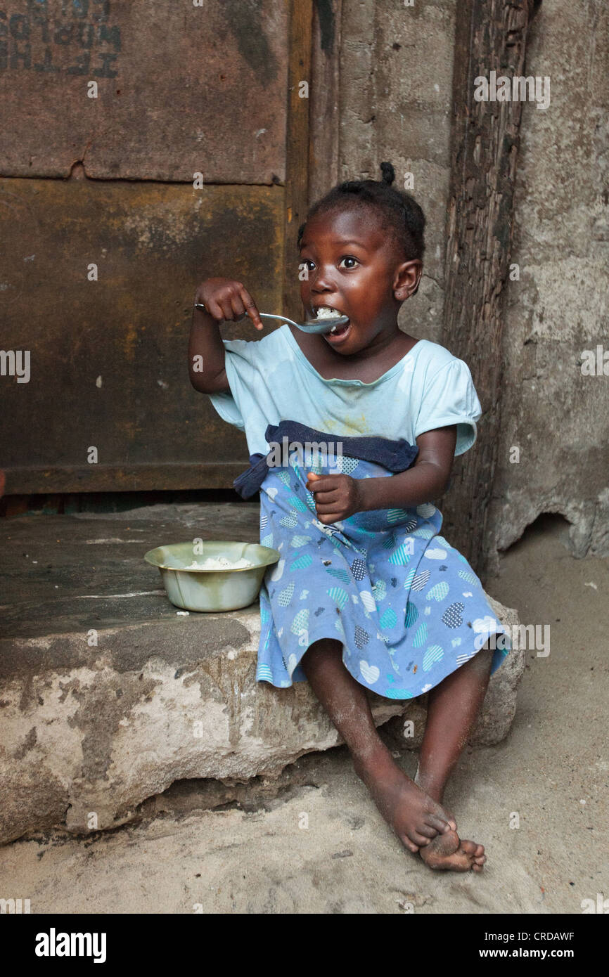 A girl eats while sitting on a doorstep in the West Point slum of Monrovia, Montserrado county, Liberia on Monday April 2, 2012. Stock Photo